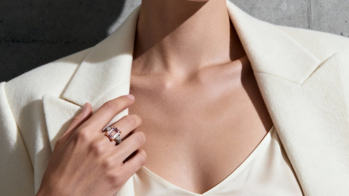 Woman wearing morganite and diamond ring a white blazer against a gray concrete wall