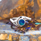 Boulder opal ring in palladium silver with a blue green opal, resting on boulder opal rough