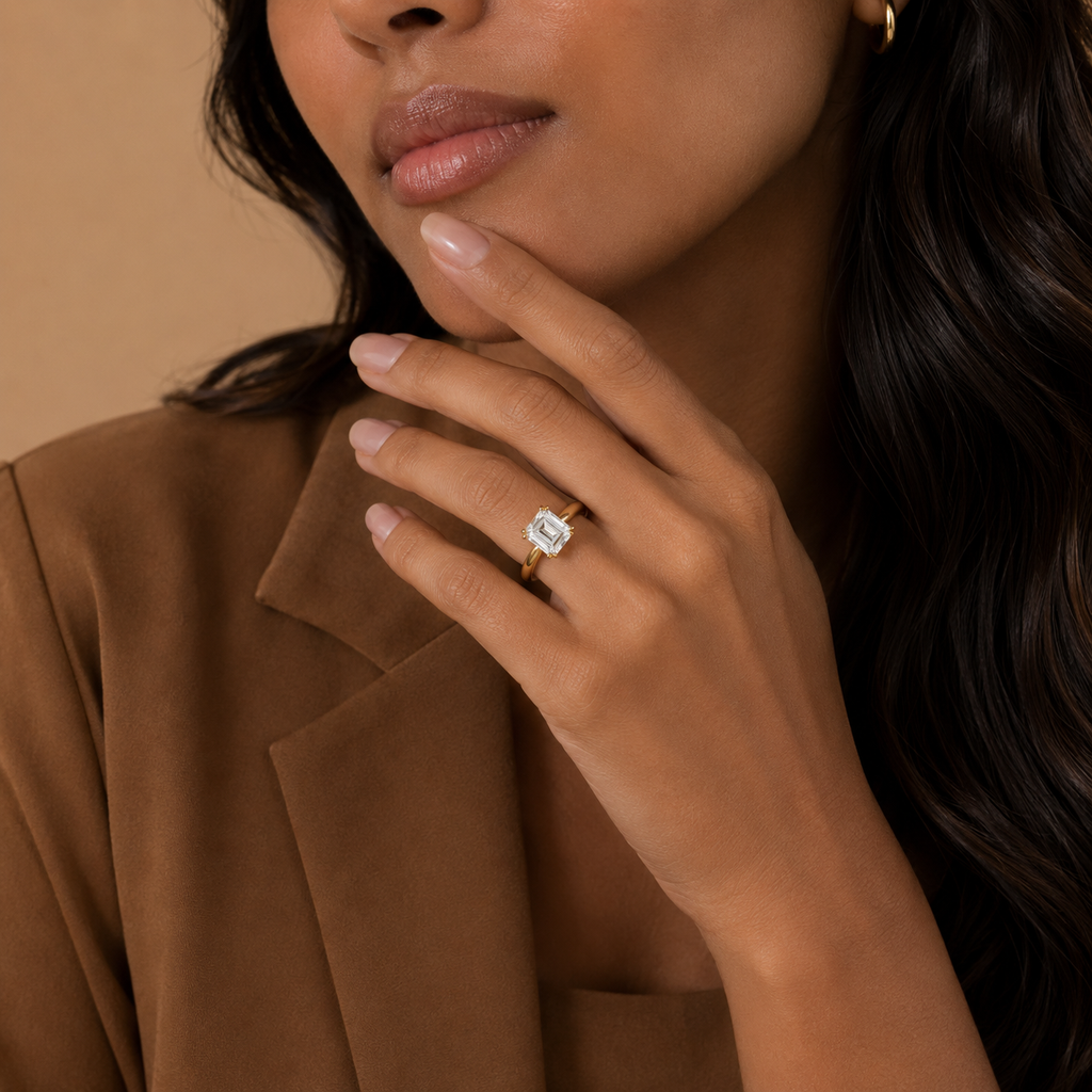 Model in a tan blazer wearing the Belle emerald cut solitaire ring, hand at the chin