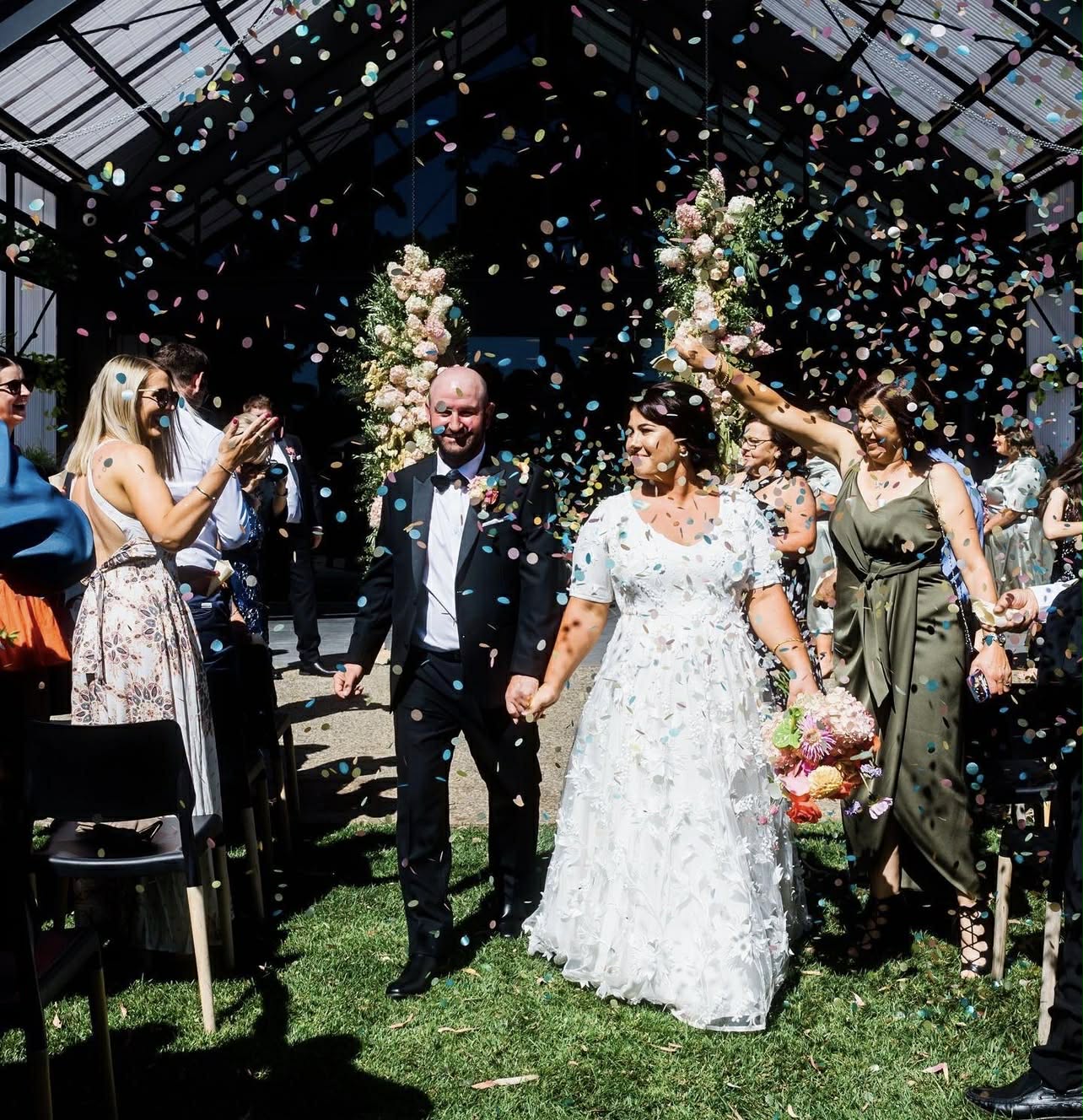Wedding couple walking under a shower of confetti with guests on either side. Metal & Stone Happy Couple Testimony